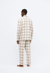Béžovo-hnedý károvaný pyžamový set vyrobený z mäkkej látky. Košeľa má golier; nohavice sú voľné s vreckami.