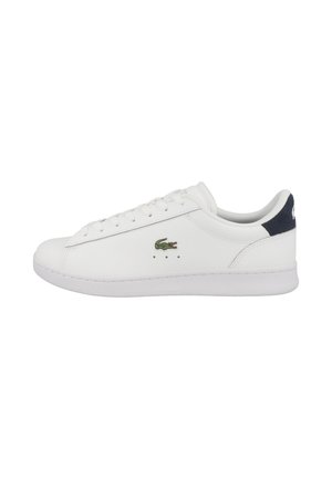 Baskets basses blanches avec lacets à l'avant, logo crocodile vert sur le côté et languette de talon bleu foncé.