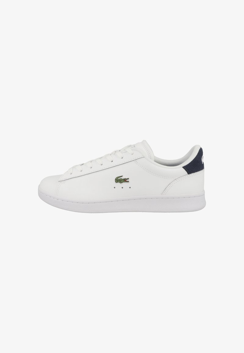 Baskets basses blanches avec lacets à l'avant, logo crocodile vert sur le côté et languette de talon bleu foncé.