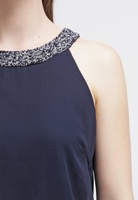 Marinblå ärmlös topp med en pärlkrage i silver- och blå nyanser, en mjuk tygkvalitet och en avkopplande passform.