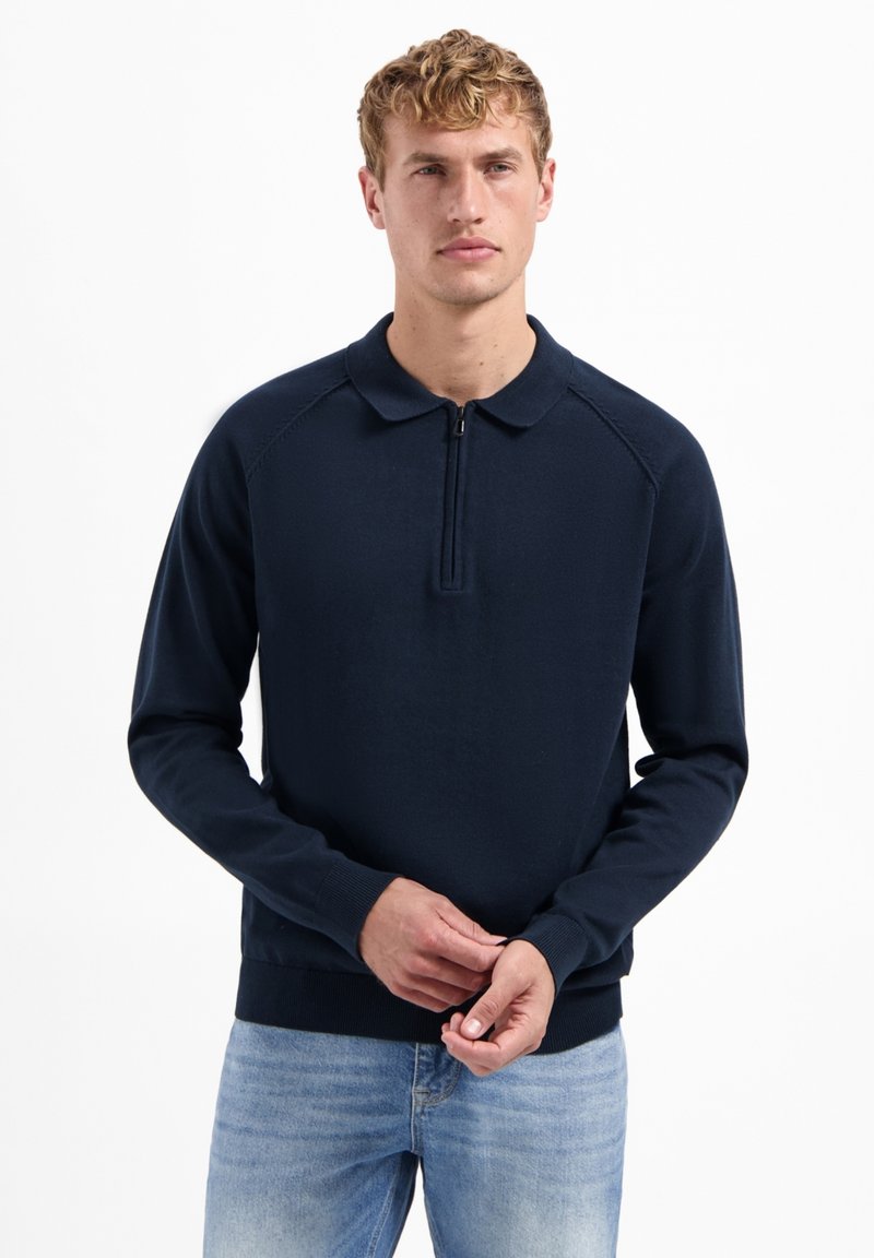 Marineblauwe pullover met een ritskraag, ribgebreide manchetten en zoom, gemaakt van een gladde gebreide stof. Heeft raglanmouwen en een minimaal ontwerp.