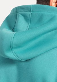 Felpa turchese con un morbido mix di cotone, cappuccio con cordino e dettagli di cucitura distintivi sui bordi.