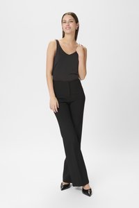Pantalons noirs ajustés à taille haute et jambes évasées, associés à un débardeur sombre. Le matériau semble lisse et extensible.