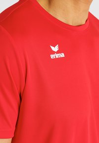 Rood shirt met korte mouwen, gemaakt van gladde, rekbare stof. Heeft een wit logo op de bovenste linkerkant. Ronde halslijn, aansluitend ontwerp.