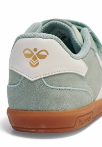 Jasnoniebieski zamszowy sneaker z białymi skórzanymi akcentami. Posiada brązową, fakturowaną gumową podeszwę oraz złote logo pszczoły na pięcie.