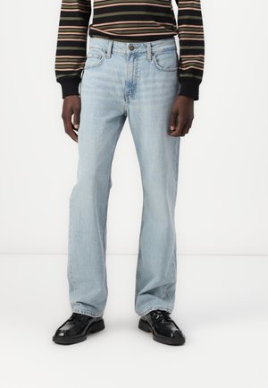 Helles blaues Denim-Jeans mit geradem Bein, Fünf-Taschen-Design und subtilen Waschungen. Getragen mit einem gestreiften schwarzen Hemd und schwarzen Schuhen.