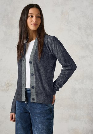 Cardigan rayé marine avec un avant à boutons, texture côtelée et manches longues, porté avec un haut blanc et un jean en denim.