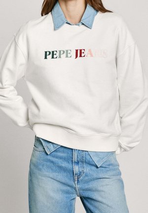 Persona vistiendo una sudadera blanca con texto multicolor "PEPE JEANS", superpuesta sobre una camisa de mezclilla azul claro y unos vaqueros azules de talle alto.