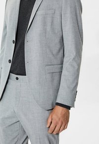 Traje gris claro hecho de tejido texturizado, que presenta un blazer de un solo botón, solapas con muescas y un bolsillo en el pecho, combinado con pantalones a juego.