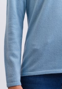 Ljusblå stickad tröja med en mjuk textur, långa ärmar och rundad nederkant. Har en enkel design utan mönster eller utsmyckningar.