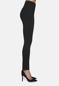 Czarne legginsy z wysokim stanem, wykonane z elastycznego materiału, o gładkiej teksturze i bocznymi kieszeniami. Noszone z czarnymi szpilkami w kształcie spiczastym.