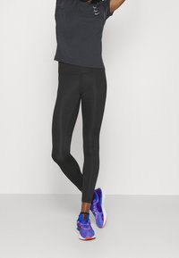 Leggings negros combinados con una camiseta de manga corta gris oscuro y zapatillas de correr multicolores presentan materiales transpirables y un diseño ajustado.