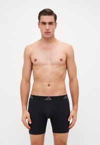 Boxer briefs pretos com uma faixa larga, apresentando detalhes em roxo. O material parece suave, com um design ajustado e comprimento até a metade da coxa.