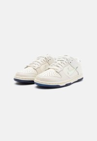 Valged nahast tenisekad, millel on perforatsioonidega varvas, iridescentne swoosh ja tumesinine kummist tald. Omab ümarat kuju ja paeltega sulgemise disaini.