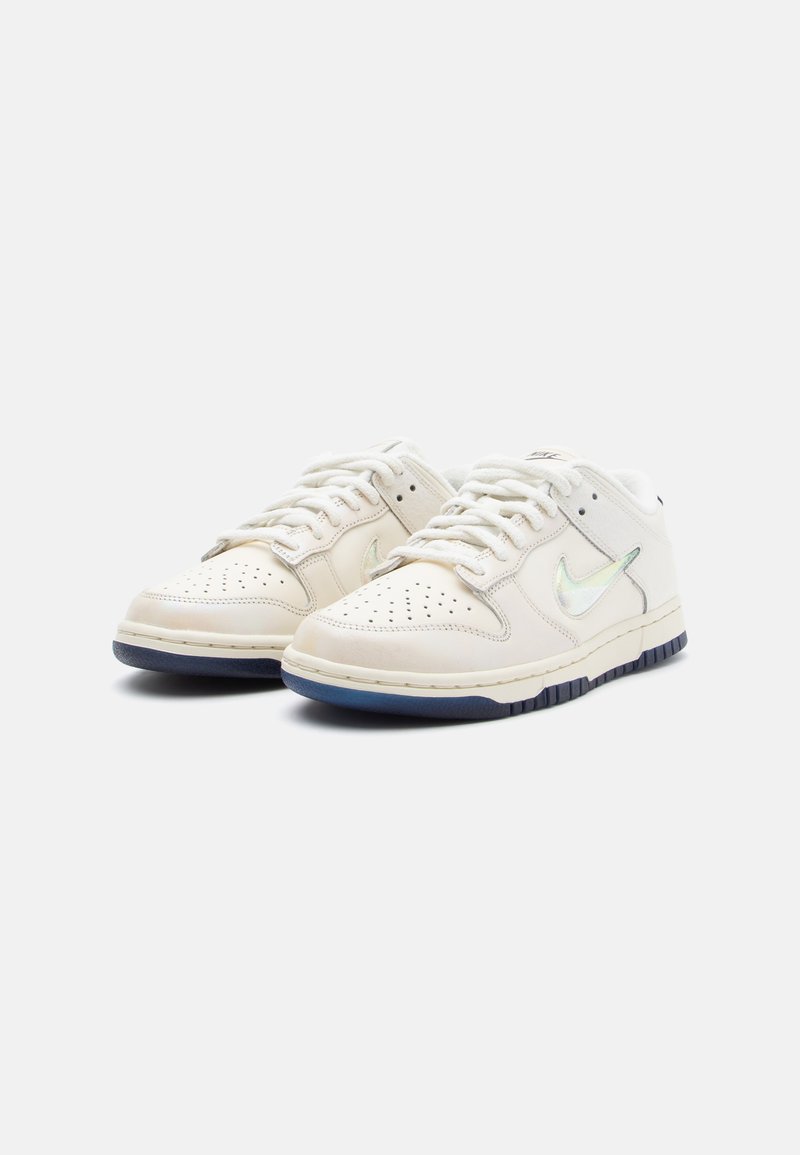 Sneakers bianchi in pelle con punta perforata, swoosh iridescente e suola in gomma blu navy. Presentano una forma arrotondata e un design con chiusura a lacci.