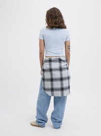 Lys blå tettsittende kortermet skjorte kombinert med løse denimjeans og en svart-hvit rutete skjorte bundet rundt livet.