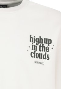 Weißes Sweatshirt aus Baumwollmischung, mit fettem schwarzen Text "hoch oben in den Wolken" und Sternen sowie "RESET TAG" in kleinerer Schrift darunter.