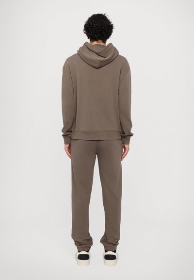 Brun hettegenser og joggebukse sett laget av myk stoff, med en avslappet passform, ribbestrikkede mansjetter og en romslig hette. Sneakers med svarte detaljer.