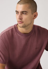 Μπορντό μπλούζα με στρογγυλή λαιμόκοψη από μαλακό βαμβάκι. Διαθέτει άνετη εφαρμογή, κοντά μανίκια και διακριτικό λογότυπο στο στήθος. Απλή, ομαλή υφή.