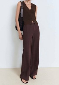 Brązowa dzianinowa kamizelka z dekoltem w serek i guziczkami, połączona z szerokimi brązowymi spodniami i płaskimi sandałami. W zestawie czarna pleciona torebka.