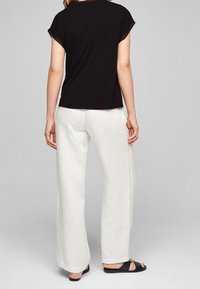 Top negro de manga corta combinado con pantalones de lino blancos de pierna ancha y sandalias negras, mostrando siluetas casuales y relajadas con texturas ligeras.