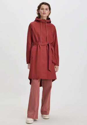 Rote Baumwolljacke mit Kapuze, Kordelzug und Gürtel. Mit langen Ärmeln,Seitentaschen und einem längeren hinteren Saum ausgestattet. Über passenden Hosen getragen.