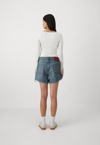 Jeanshorts med franset kant og en rød "HUGO"-lapp bak. Kombinert med en tettsittende hvit langermet topp og hvite sokker.