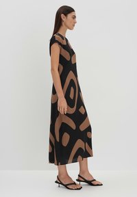 Maxikleid aus leichtem Stoff mit schwarzem Grund und abstrakten braunen Mustern. Ärmellos mit lockerer Passform; kombiniert mit schwarzen Riemchensandalen.
