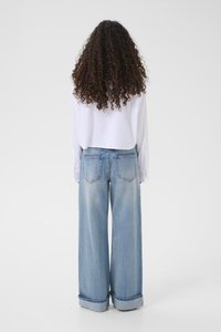 Biała koszula z długim rękawem włożona w szerokie, jasnoniebieskie dżinsy typu wide-leg, o luźnym kroju i podwiniętych mankietach, widziana od tyłu.