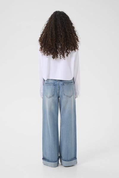 Chemise blanche à manches longues rentrée dans un jean large en denim bleu clair, avec une coupe décontractée et des revers de manches roulés, vue de dos.