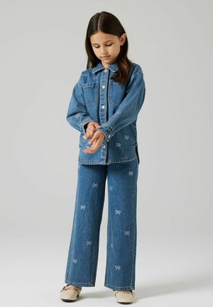 Tenue en denim composée d'une veste boutonnée et d'un pantalon à jambes larges, tous deux ornés de motifs de nœuds blancs brodés. Teinte bleu clair, texture douce.