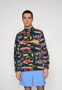 Maglione in pile con base verde, caratterizzato da un motivo di pesci colorati in rosso, blu e giallo. Include una tasca color nocciola e un design con collo alto.