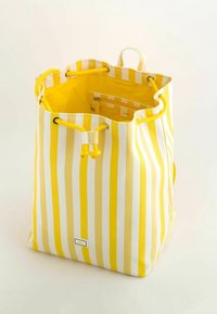 Keltainen ja valkoinen pystysuora raidoitettu kangaskassi, jossa on kiristysnauha ja sisempi vetoketjullinen pussi, esitetty avoimena vaaleaa taustaa vasten.
