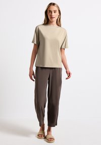 Beige top s krátkým rukávem a uvolněným střihem, s dekorativními akcenty podél výstřihu. V kombinaci s hnědými, lehkými, taperovanými kalhotami.