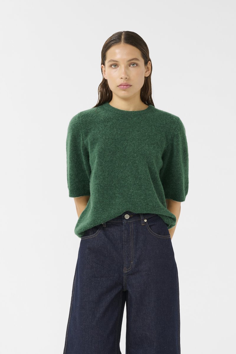 Green wool sweater with short sleeves, round neckline, and soft texture, paired with dark denim wide-leg jeans featuring front pockets.