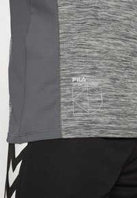 Maglietta atletica grigia con tessuto testurizzato, pannelli di design a contrasto e logo Fila bianco. Abbinata a pantaloni corti neri con accenti bianchi.