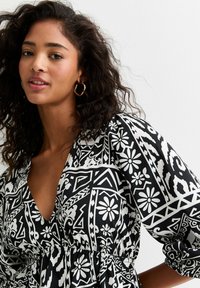 Robe à motifs en noir et blanc avec des motifs floraux et géométriques, dotée d'un décolleté en V et d'une taille élastique, fabriquée en tissu lisse.