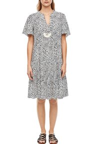 Kortärmad klänning i vitt med svart leopardmönster, med V-ringning och volangkjol. Accessoarer med en dekorativ hängande halsband.