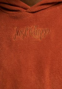Oranžen flis hudournik z mehkobo in kenguru žepom. Ima izvezen logo "JustRhyse" spredaj v kontrastni barvi.