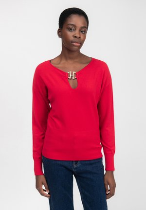 Maglione rosso con scollatura a V e dettaglio a chiave, caratterizzato da un accento in metallo a gancio. Maniche lunghe e orlo a coste per texture.