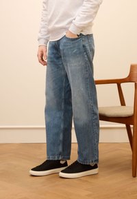 Light blue denim jeans with a loose fit, faded texture, and straight legs. Paired with black sneakers and a gray sweatshirt.