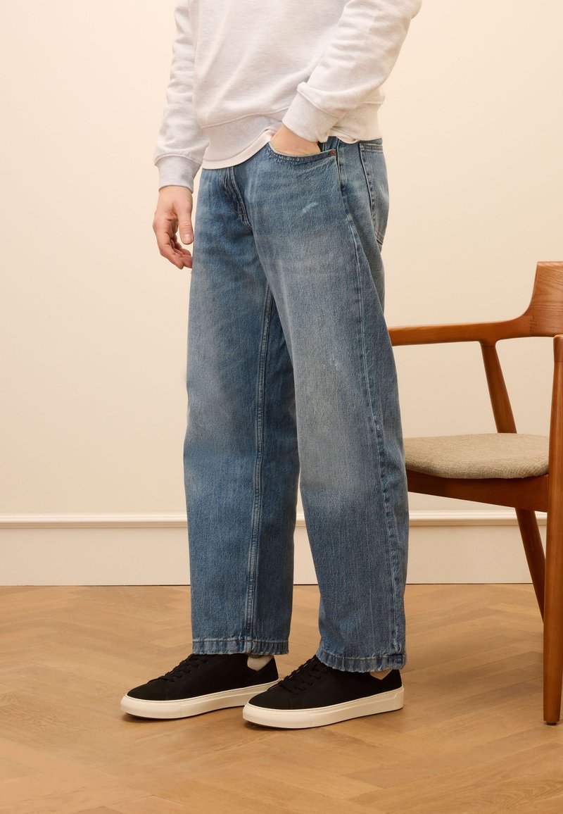 Light blue denim jeans with a loose fit, faded texture, and straight legs. Paired with black sneakers and a gray sweatshirt.