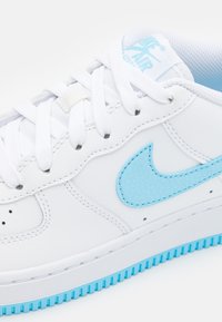 Fehér sneaker világoskék részletekkel. Simaszerű bőrből készült, textúrázott swoosh-tal és világoskék mintázatú gumitalppal rendelkezik.