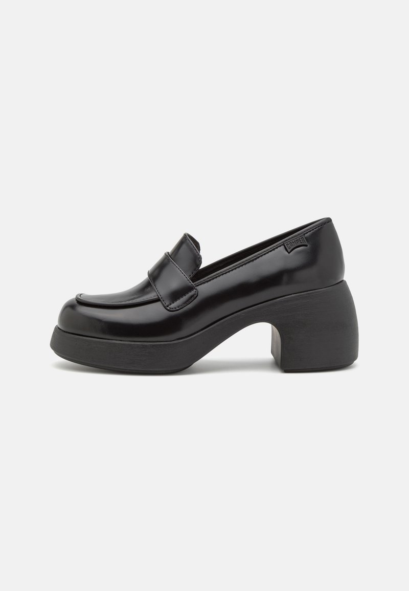 Loafers en cuir verni noir avec un embout rond, une sangle frontale proeminente et un large talon noir. Texture lisse, détails minimaux.