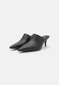 Mules en cuir noir avec un bout pointu, un petit talon et une texture lisse. Le design élégant présente un dos ouvert et une esthétique minimaliste.