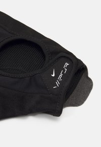 Sort atletisk beklædning med en tekstureret overflade, prydet med en cirkulær udsparing, elastiske kanter og et lille hvidt Nike-logo. Glat, fleksibelt materiale.