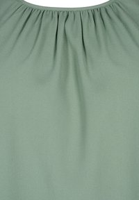 Blusa verde menta realizzata in tessuto morbido e fluido, con texture arricciata sul collo, che offre una vestibilità rilassata e un aspetto uniforme.