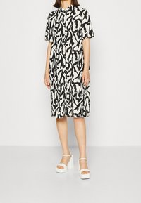 Kurzarmkleid mit einem weißen und schwarzen abstrakten Muster, ausgestattet mit Knopfleiste vorn, lockerem Schnitt und kombiniert mit weißen Plateau-Sandalen.