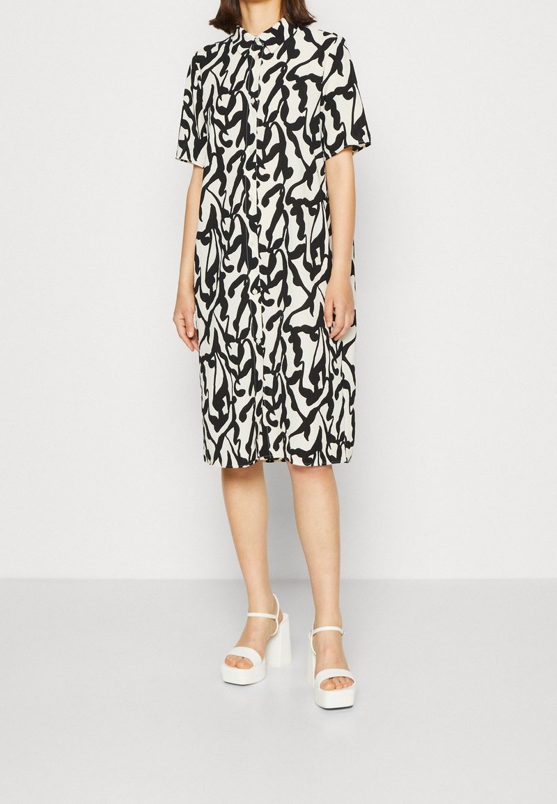 Kurzarmkleid mit einem weißen und schwarzen abstrakten Muster, ausgestattet mit Knopfleiste vorn, lockerem Schnitt und kombiniert mit weißen Plateau-Sandalen.