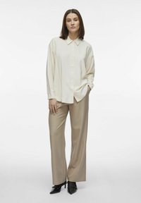 Camisa crema de botones con cuello, combinada con pantalones de pierna ancha beige y tacones de punta negra. Tela suave, ajuste relajado.